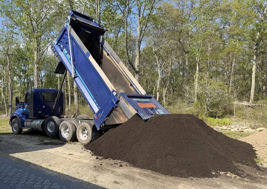 Blue dump truck unloading a large topsoil pile