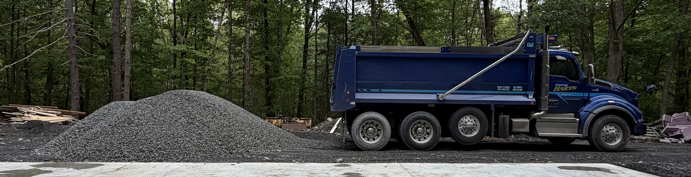 Tri-axle dump truck staged beside a fresh stone delivery