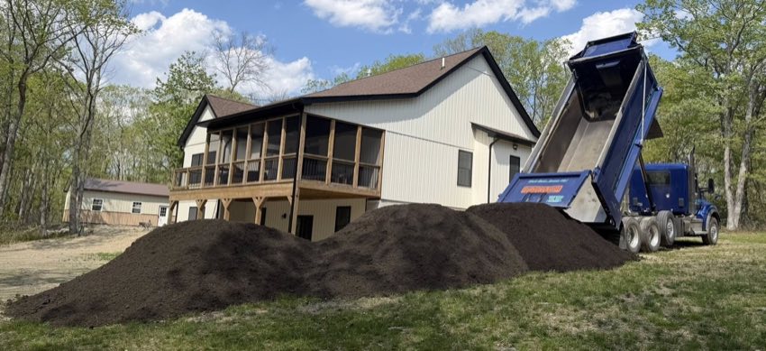 Dump truck delivering topsoil near a home
